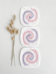 three crocheted coasters sitting on top of a table next to a dried plant