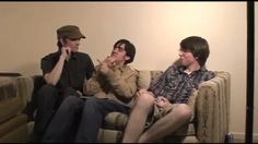 three young men sitting on a couch talking to each other