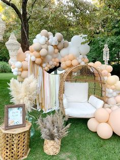 an outdoor party with balloons and decorations on the grass, including a wicker chair