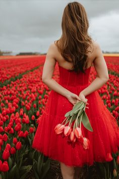 a woman in a red dress standing in a field of tulips with her back to the camera