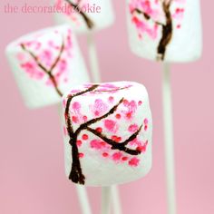 marshmallows decorated with pink and brown cherry blossoms on a white stick in front of a pink background