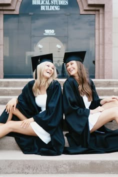 two women in graduation gowns sitting on steps