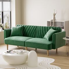 a green couch sitting in a living room next to a white table and vases