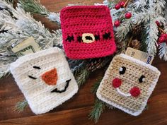 three crocheted mug cozyies sitting on top of a wooden table next to pine branches