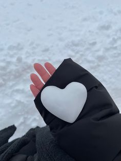 a person's hand with a white heart on it in front of snow covered ground