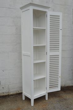 a tall white cabinet with shutters on the front and bottom doors is standing against a brick wall