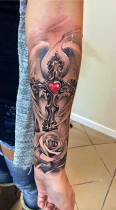 a woman's arm with a cross and roses tattoo on her left forearm,