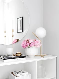 a white table with flowers and a mirror on it's wall above the bookshelf