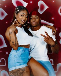 a man and woman posing for a photo with hearts on the wall in the background