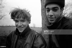 two young men standing next to each other in front of a tree with no leaves