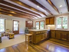 a large open kitchen and living room with wood beams on the ceiling, hardwood flooring, and white walls