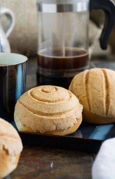 two rolls on a black plate next to a cup of coffee and a teapot