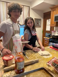 a young man and woman preparing food in the kitchen with ingredients on the counter top