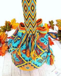 an orange, blue and yellow bag sitting on top of a wooden floor next to autumn leaves