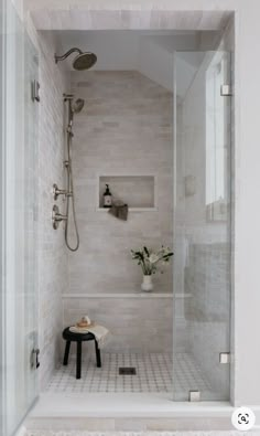 a walk in shower sitting next to a white tiled wall and floor with a black stool