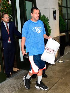 a man in blue shirt and shorts carrying a white bag while walking down the street