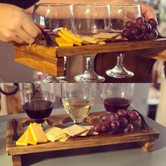 three glasses of wine, cheese and grapes on a wooden tray with two people pouring them