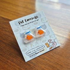 two little goldfish earrings sitting on top of a wooden table next to a card