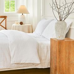 a bed with white linens and pillows in a bedroom next to a lamp on a table