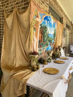 a long table with plates on it in front of a painting and brick wall behind it