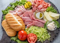 an assortment of meats and vegetables on a platter with bread, tomatoes, lettuce