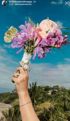 a person holding a bouquet of flowers up to the sky with palm trees in the background