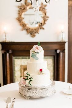 a white wedding cake sitting on top of a silver platter next to a chandelier