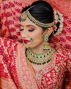 a woman wearing a red and gold bridal outfit with jewelry on her head,