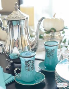 a table topped with blue glass dishes and silver teapots on top of it