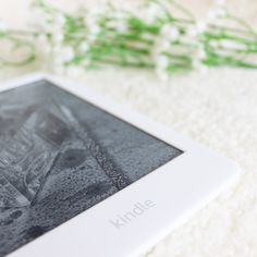 a kindle sitting on top of a white rug next to flowers and a green plant