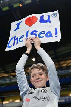 a young boy holding up a sign with the words i love you chelsea on it