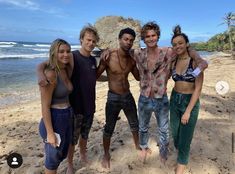 a group of young people standing on top of a sandy beach next to the ocean