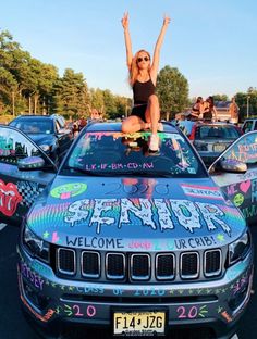 a woman sitting on the hood of a car with her arms up in the air