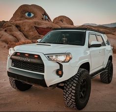 a white toyota suv parked in front of a rock formation with an evil face on it