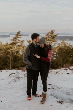 a man and woman standing in the snow with their arms around each other looking at something