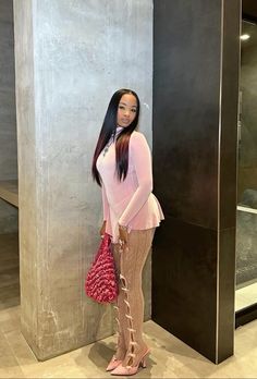 a woman standing in front of a wall holding a red purse and posing for the camera