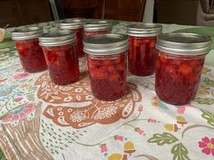 six jars filled with jelly sitting on top of a floral table cloth covered tablecloth