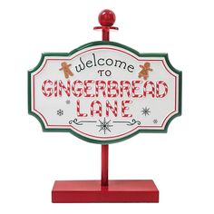 a welcome sign for gingerbread lane is displayed on a red stand with snowflakes