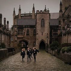 three children are running down the cobblestone road in front of an old building