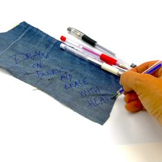 someone is writing on a piece of fabric with two pens