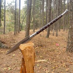 a large knife sitting on top of a piece of wood in the middle of a forest