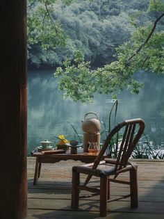 there is a table and chair on the deck by the water with a tea kettle