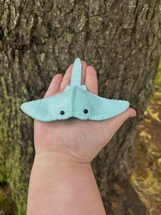 a hand holding a small blue origami bird on it's palm next to a tree