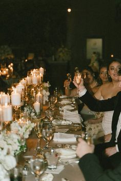 a group of people sitting at a long table with candles on the table and plates in front of them