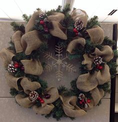 a christmas wreath hanging on the side of a wall with pine cones and holly berries