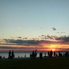 many people are walking on the beach at sunset