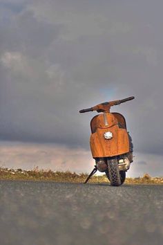 an orange scooter is parked on the side of the road under a cloudy sky