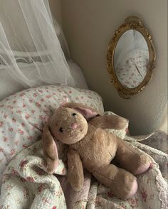 a teddy bear sitting on top of a bed next to a mirror and blanket with pink flowers