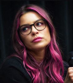 a woman with pink hair and glasses holding a microphone