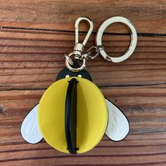 a yellow and black bee shaped keychain hanging from a wooden table with a pair of scissors